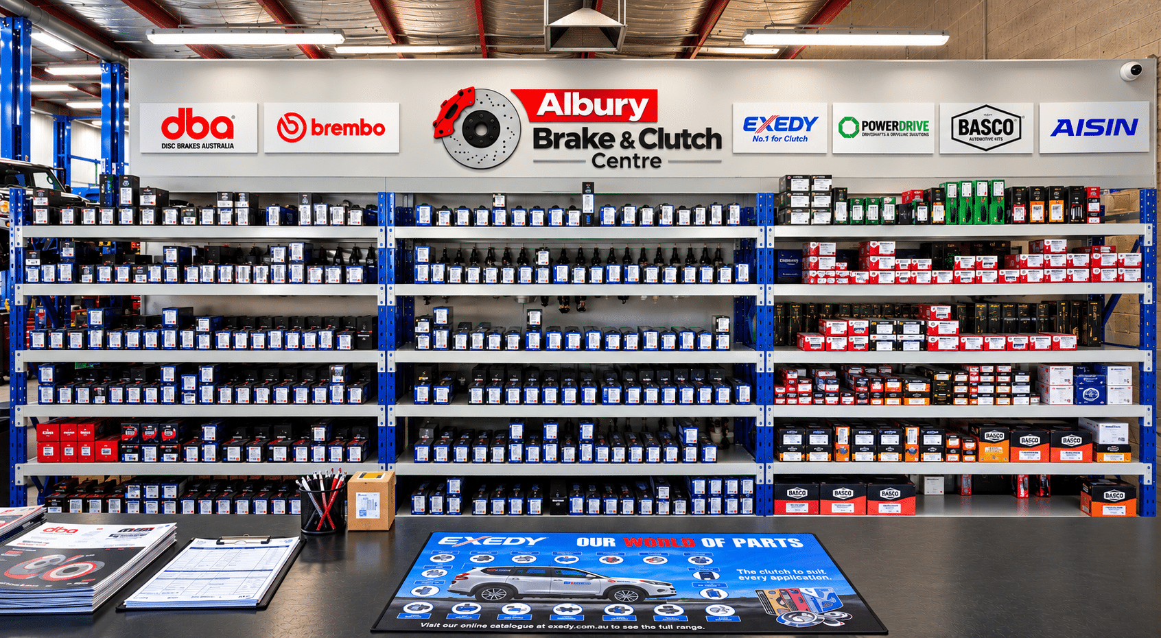 Shelving units filled with automotive parts in boxes behind a counter at Albury Brake & Clutch Centre, with an Exedy branding mat on the desk.